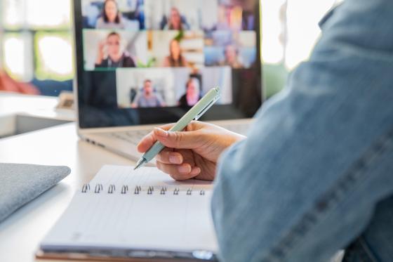 Woman taking notes while attending a virtual conference.