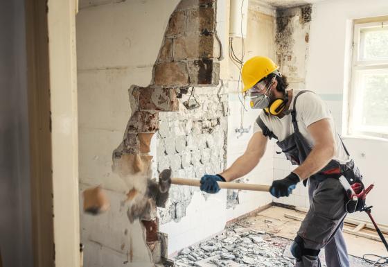 Contractor demolishing wall with sledgehammer 
