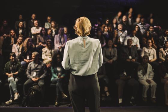 Blonde woman speaking to a large group at a conference